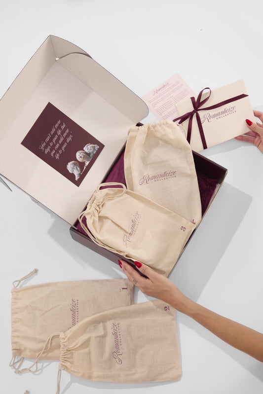 Open Romanticize Collective box holding one wrapped experience, a muslin bag tied with burgundy ribbon and a Single Experience welcome card